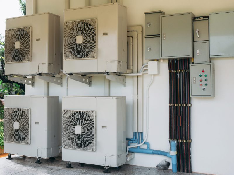 A row of air conditioners are mounted on a wall. The air conditioners are white and have a fan on top